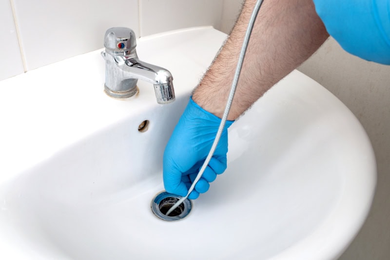 Why Do My Drains Keep Clogging? Plumbing issues, occupation in sanitation and handyman contractor concept with plumber repairing drain with plumbers snake (steel spiral that twists through pipes to collect dirt) in residential sink.
