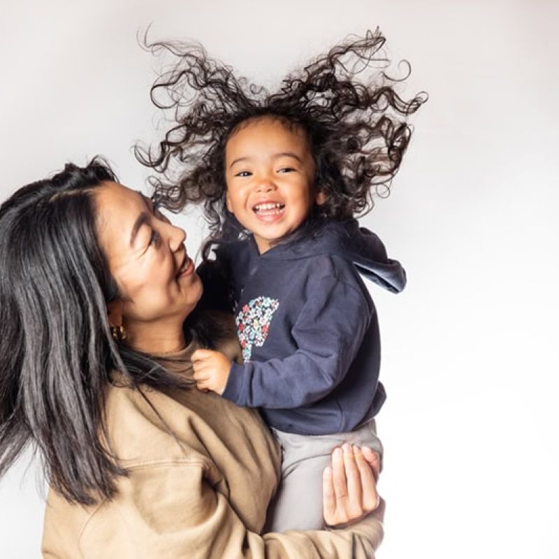 Mother holding smiling child with curly hair against a white background.