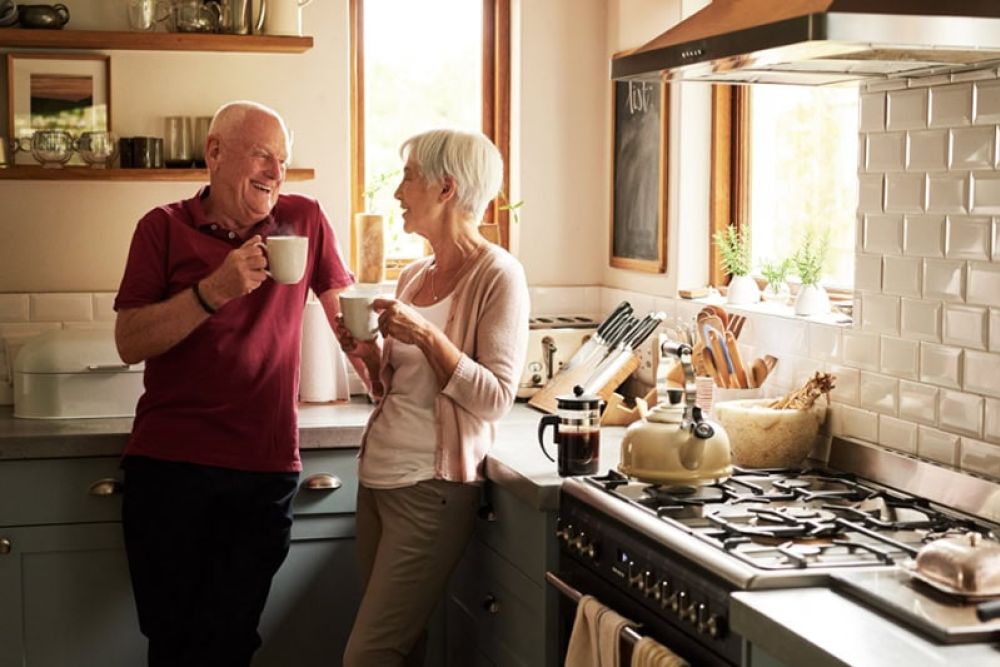 Elderly couple enjoying coffee together in a cozy kitchen with natural light and modern appliances.