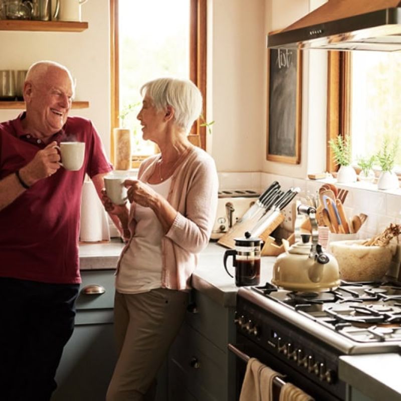 Elderly couple enjoying coffee together in a cozy kitchen with natural light and modern appliances.