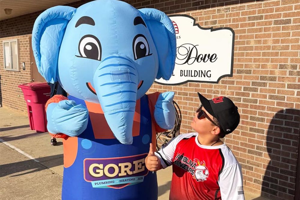 Boy gives thumbs up to cheerful elephant mascot outside building.