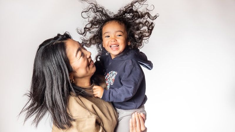 Mother holding smiling child with curly hair against a white background.