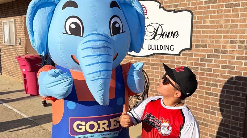 Boy gives thumbs up to cheerful elephant mascot outside building.