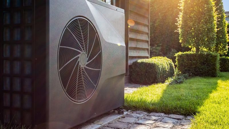 Outdoor heat pump beside a house on a sunny day, highlighting energy-efficient heating and cooling technology.