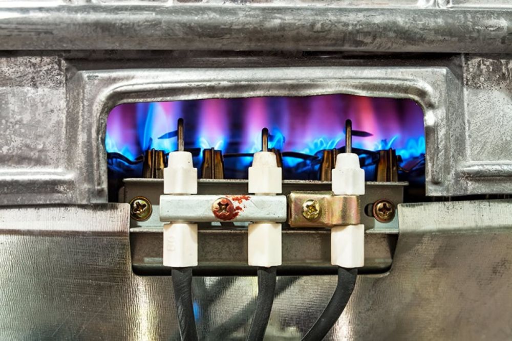Close-up of a gas burner with blue flames, showcasing industrial heating elements and metallic components.