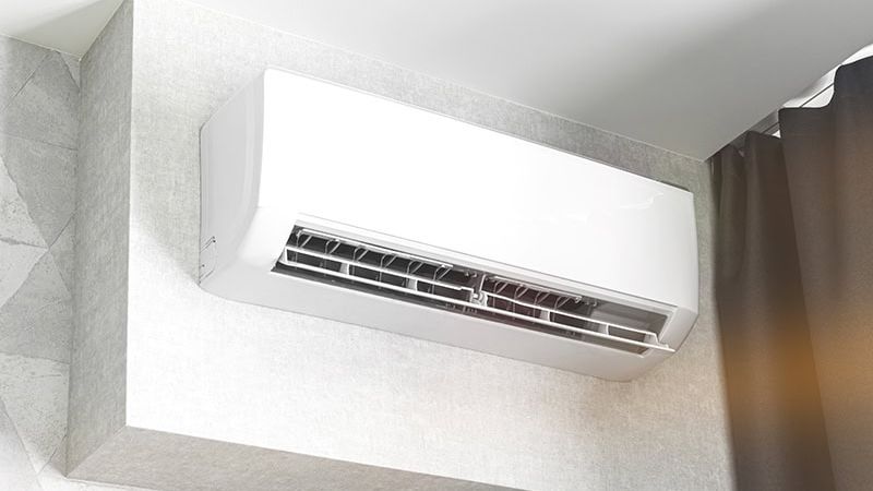 Wall-mounted air conditioning unit in modern room with gray curtains and minimalist decor.