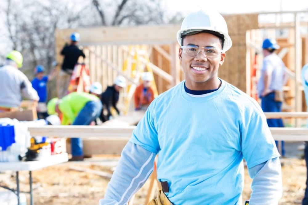 Construction worker smiling at a housing project site with team in the background.
