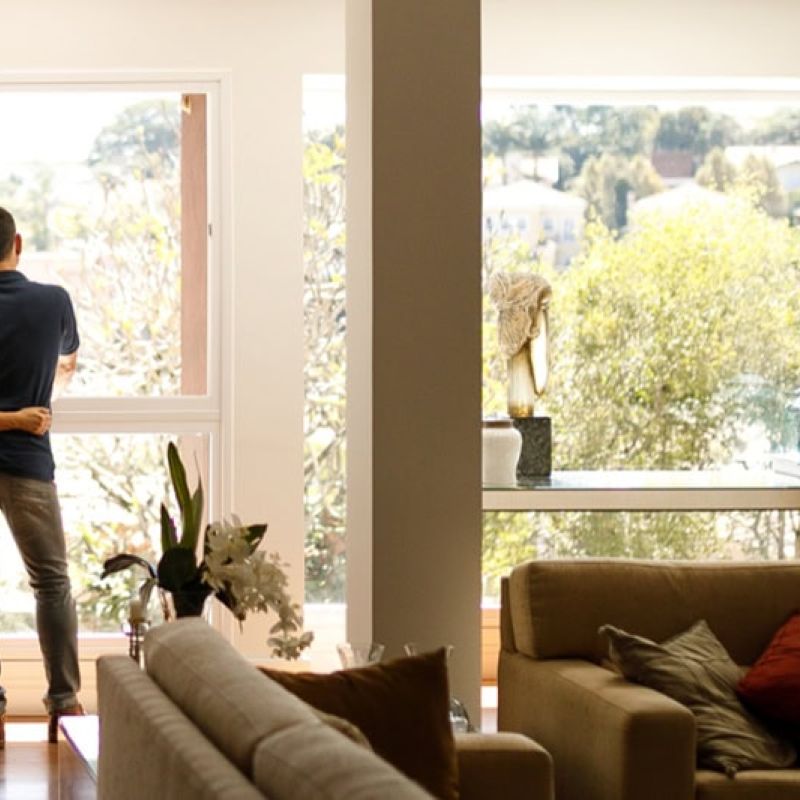 Couple embracing by large window, enjoying serene view, with cozy living room setting in foreground.