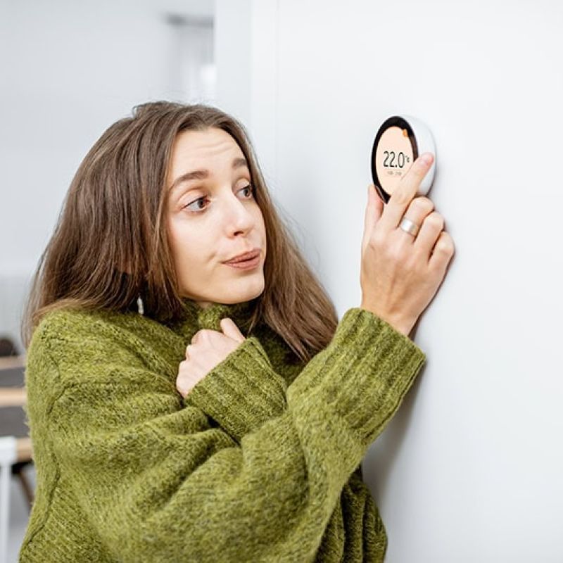 Woman in green sweater adjusts smart thermostat on wall for temperature control.