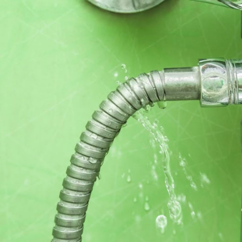 Leaking metal hose with water dripping from a pipe against a green background. Plumbing repair needed.