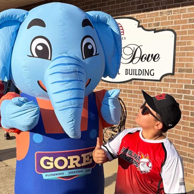 Boy gives thumbs up to cheerful elephant mascot outside building.