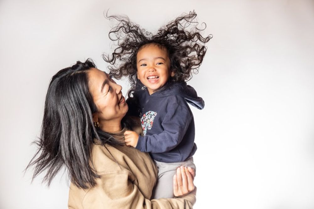 Mother holding smiling child with curly hair against a white background.