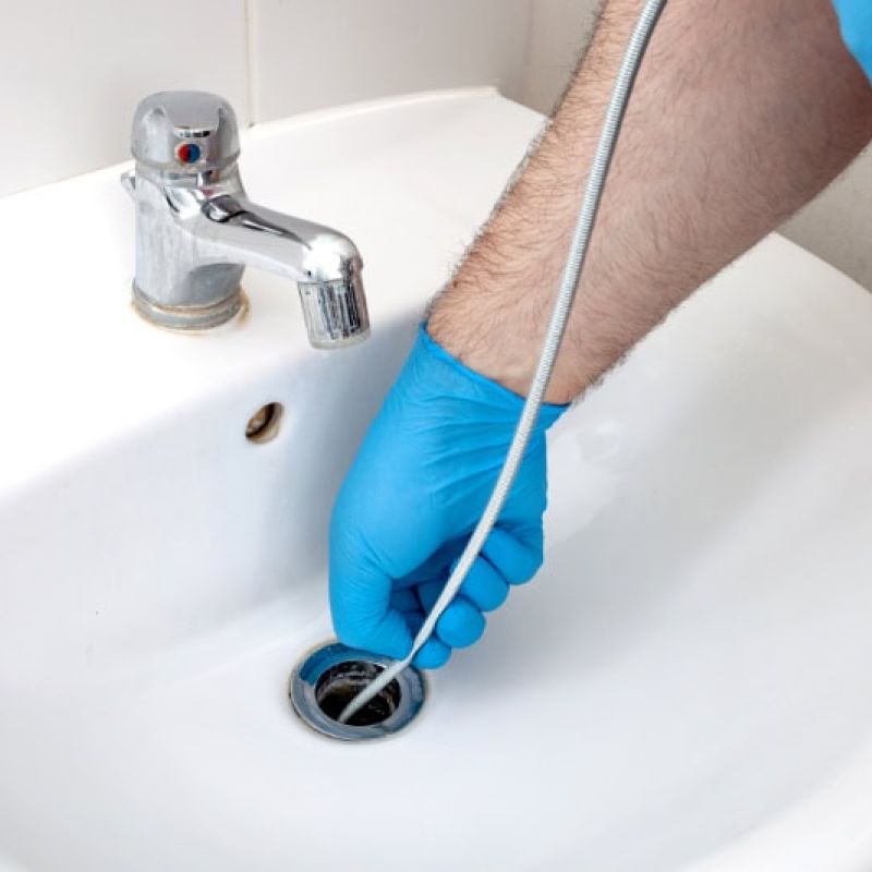 Plumber using a drain snake to unclog a bathroom sink with blue gloves.