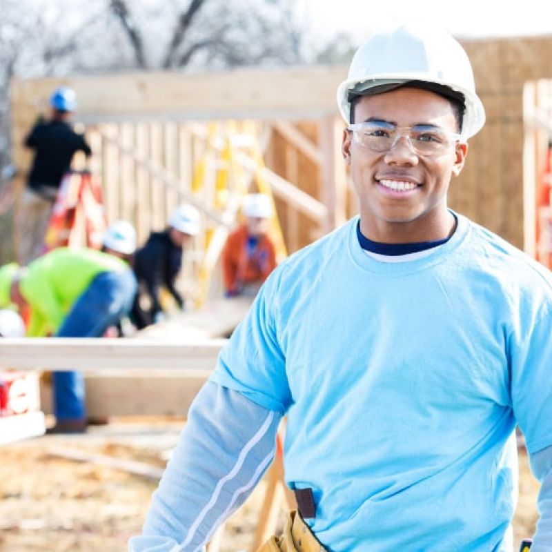 Construction worker smiling at a housing project site with team in the background.