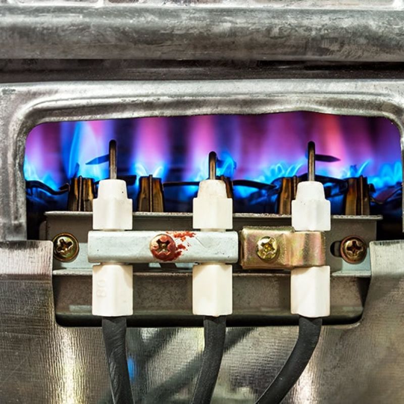 Close-up of a gas burner with blue flames, showcasing industrial heating elements and metallic components.