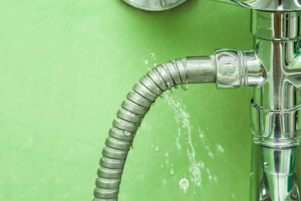 Leaking metal hose with water dripping from a pipe against a green background. Plumbing repair needed.
