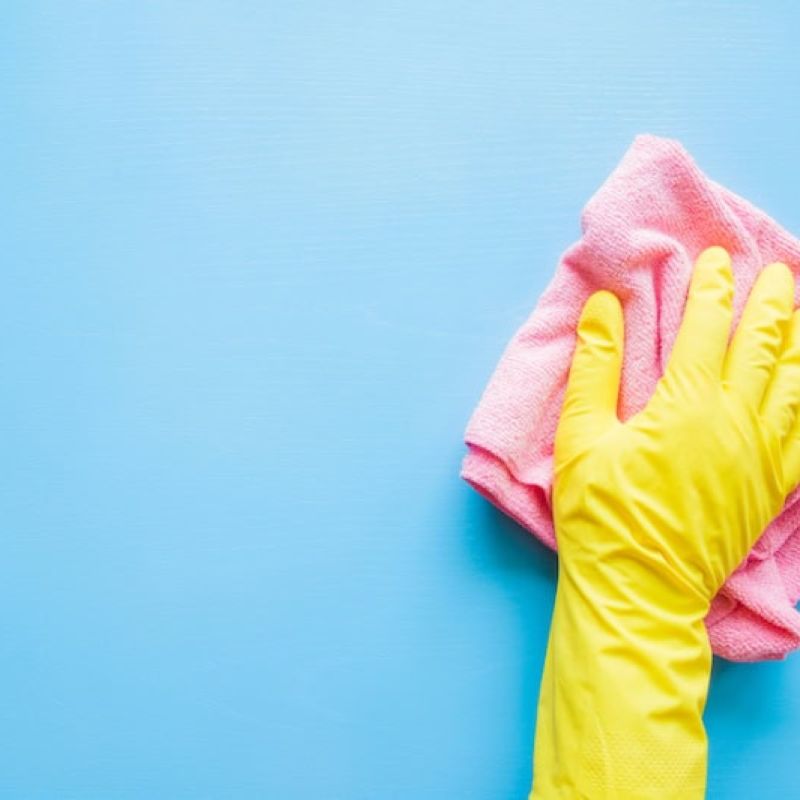Gloved hand cleaning blue surface with pink cloth for housekeeping and hygiene concepts.