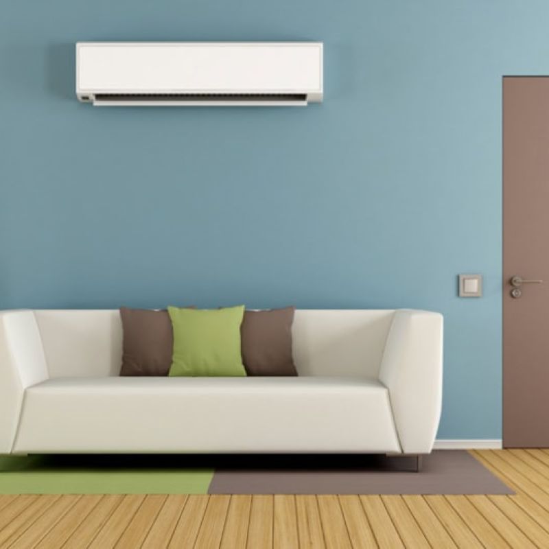 Modern living room with sofa, blue wall, air conditioner, and stylish door. Cozy decor with green and brown cushions.