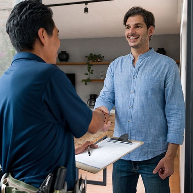 Handyman greeting homeowner with a handshake at the door, clipboard in hand. Home service interaction.