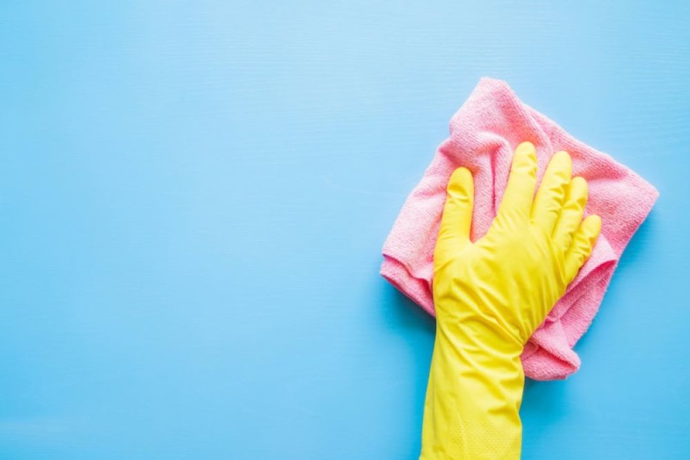 Gloved hand cleaning blue surface with pink cloth for housekeeping and hygiene concepts.
