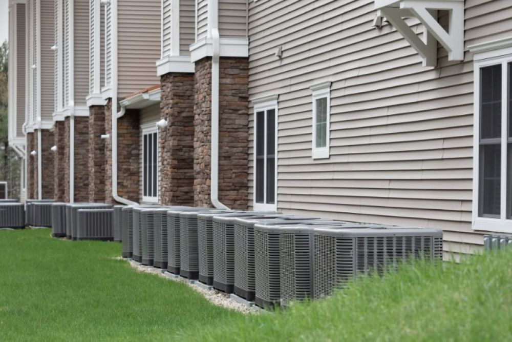 Row of outdoor air conditioning units lined up against residential building for cooling efficiency.