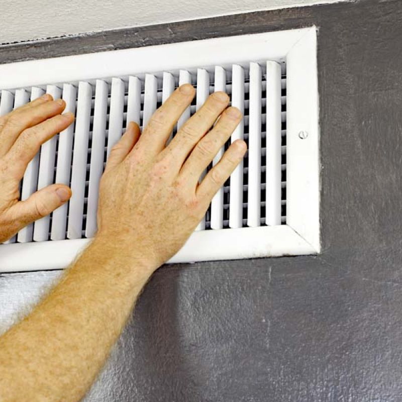 Hands adjusting a white air vent on a gray wall for improved airflow in a home or office environment.