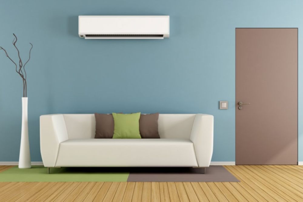 Modern living room with sofa, blue wall, air conditioner, and stylish door. Cozy decor with green and brown cushions.