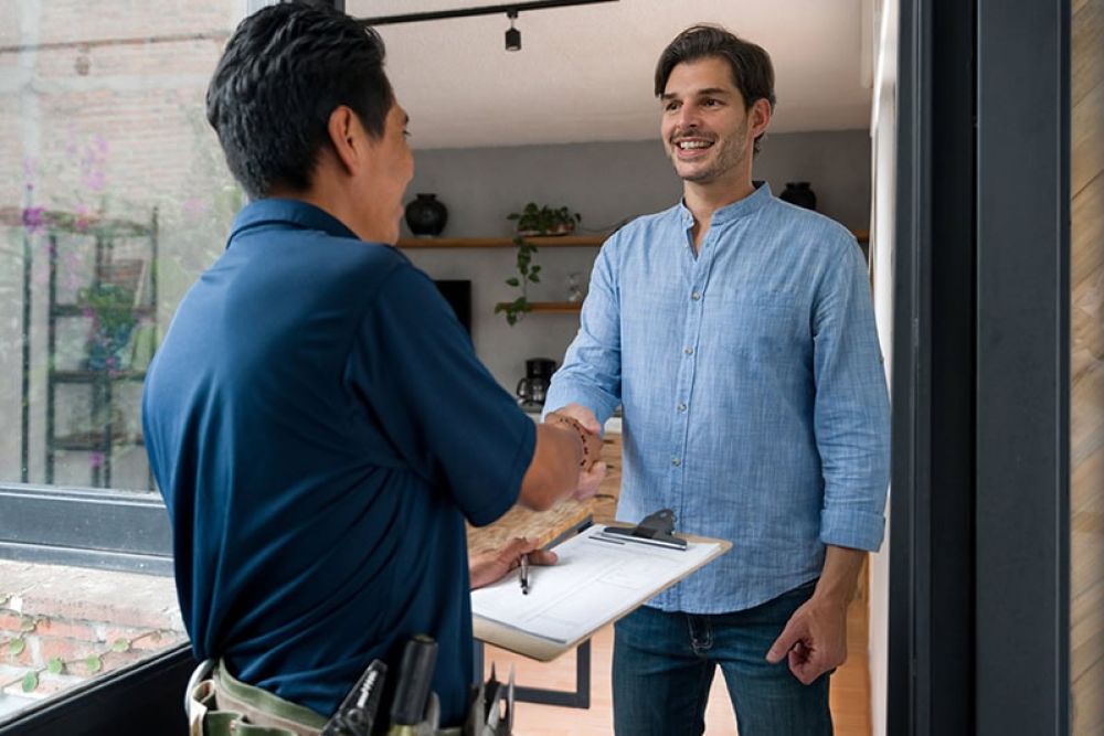 Handyman greeting homeowner with a handshake at the door, clipboard in hand. Home service interaction.